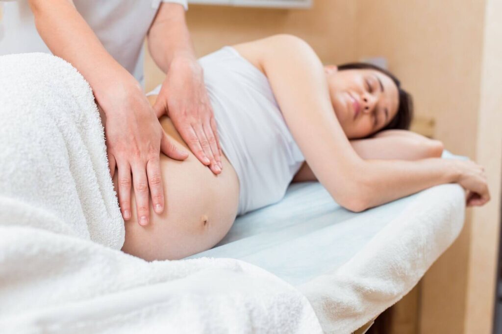 beautiful-pregnant-brunette-with-long-hair-lies-her-side-reception-with-massage-therapist-cosmetology-room (1)